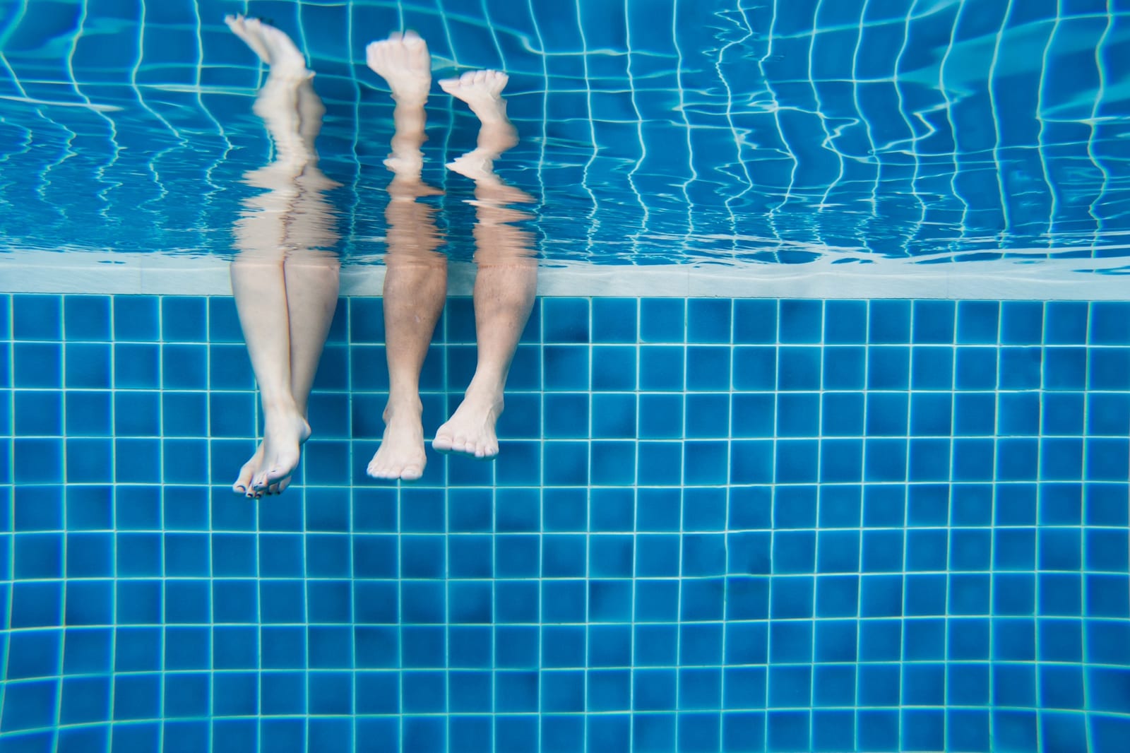 Family members' legs underwater during a summer pool day